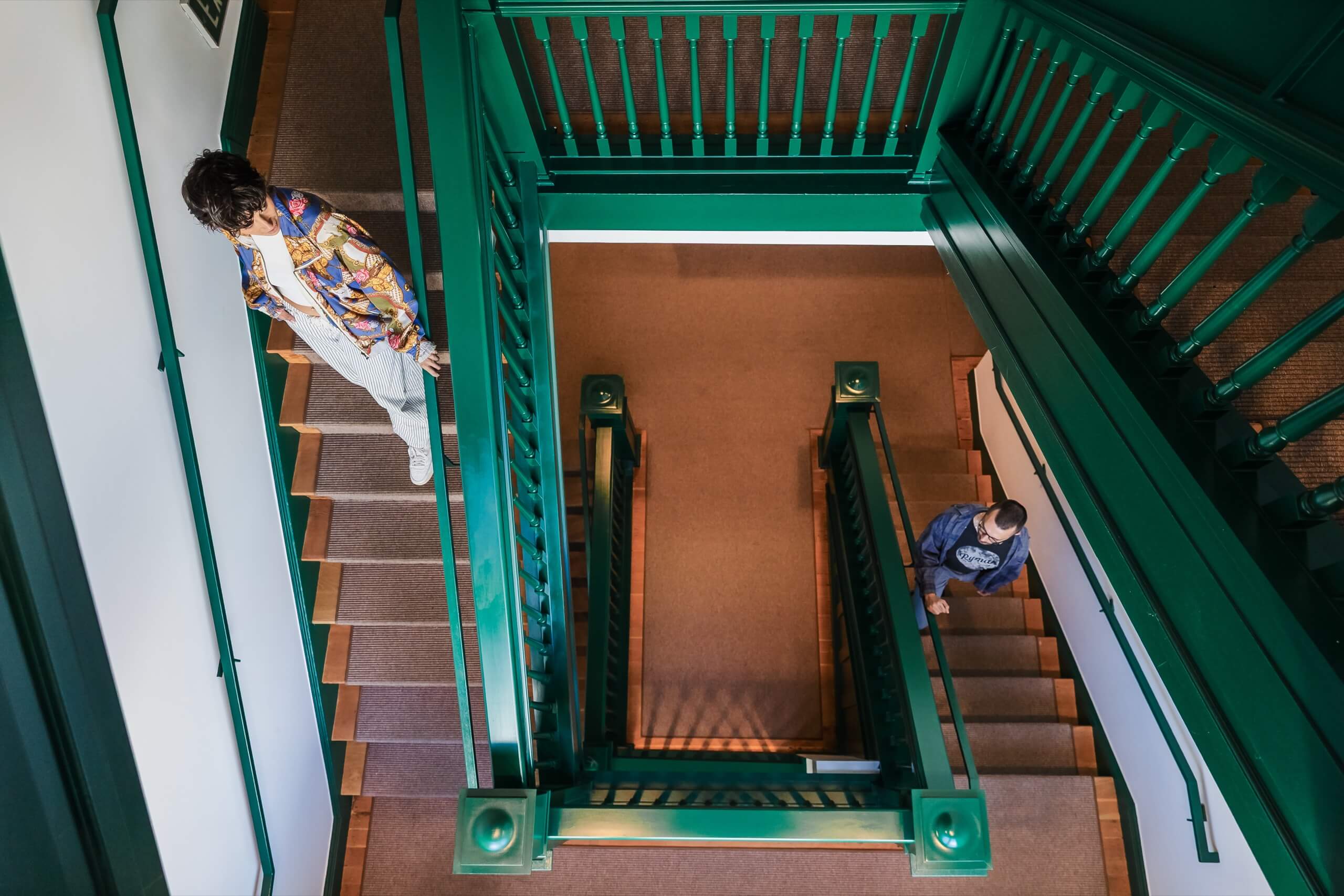 A staircase with green railings and carpeted steps, with two people on the stairs.