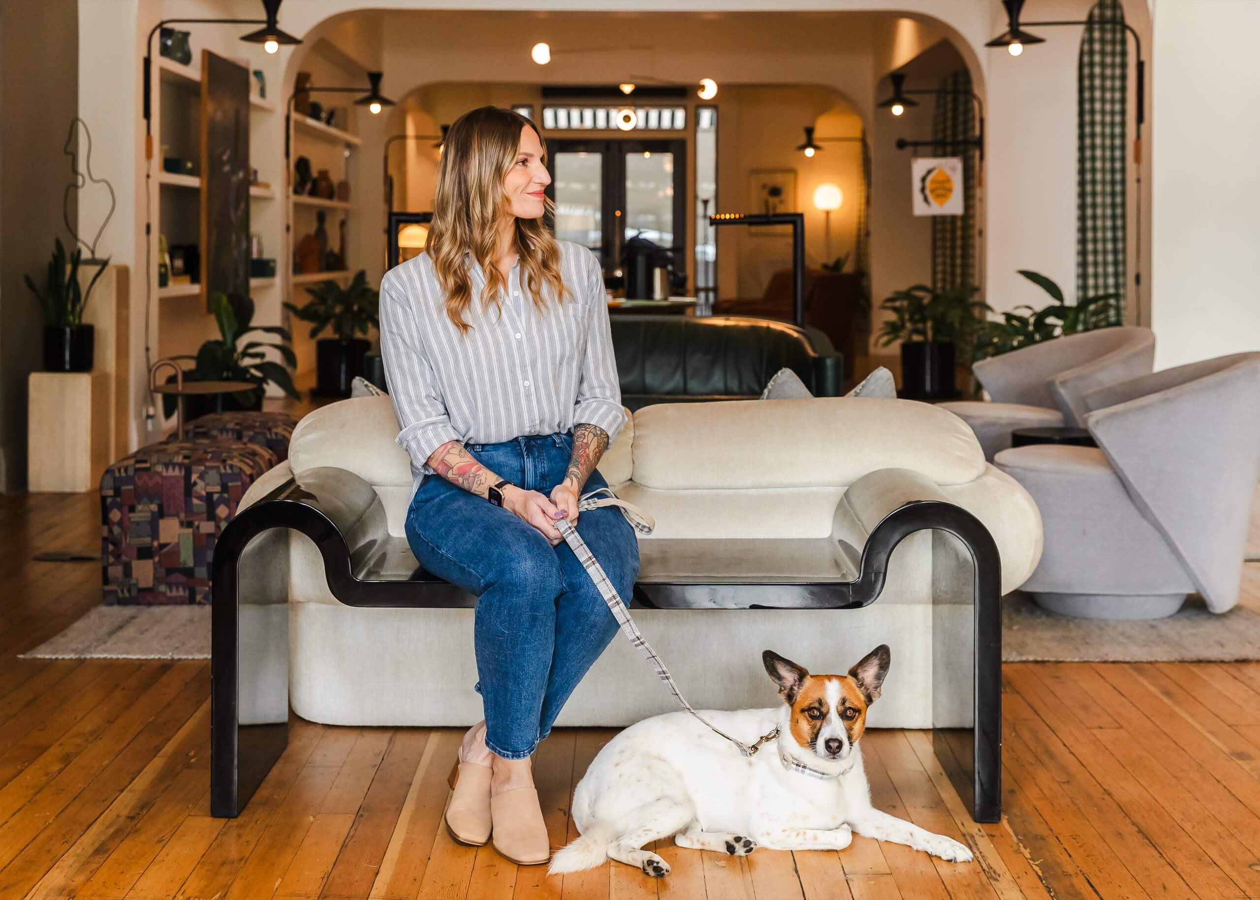 A woman sits on a sofa with a dog in a lobby area with modern furniture and decor.