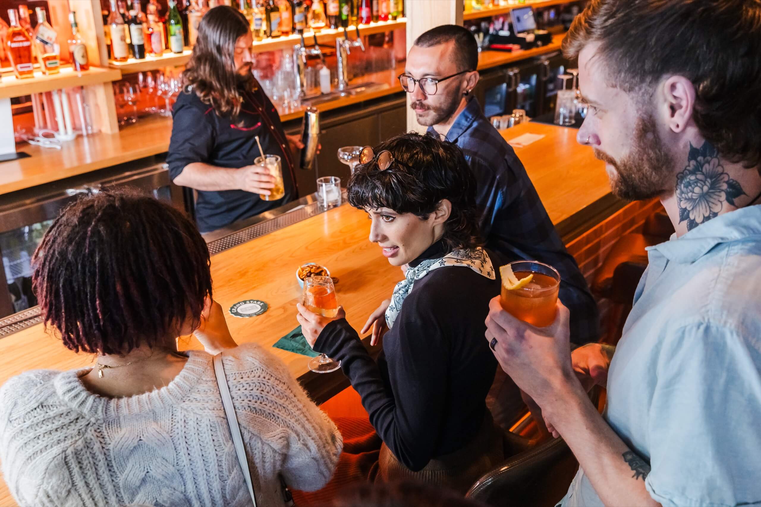 A group of people sitting at a bar, engaged in conversation and holding drinks.