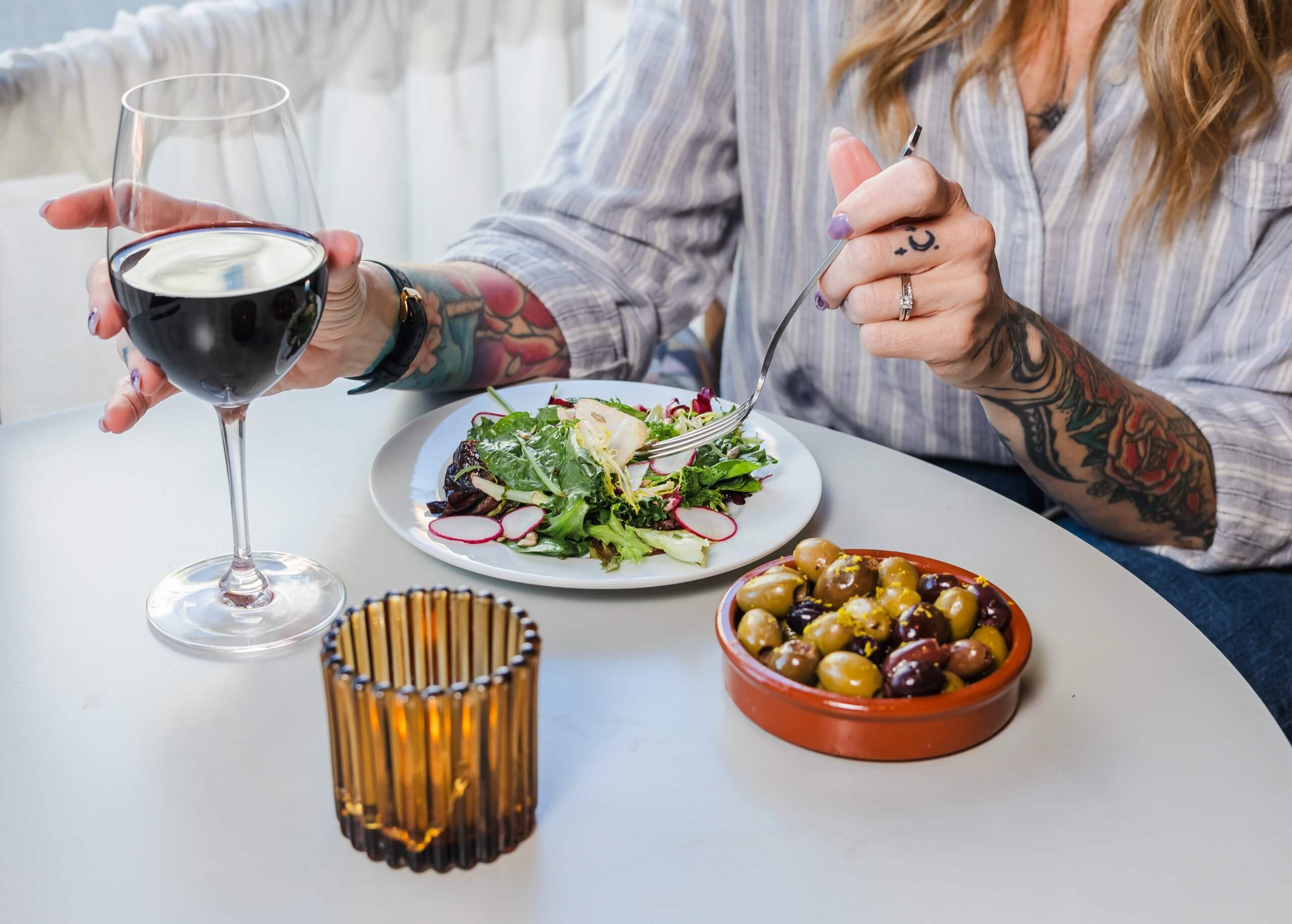 A person eating a salad and drinking wine at a table.