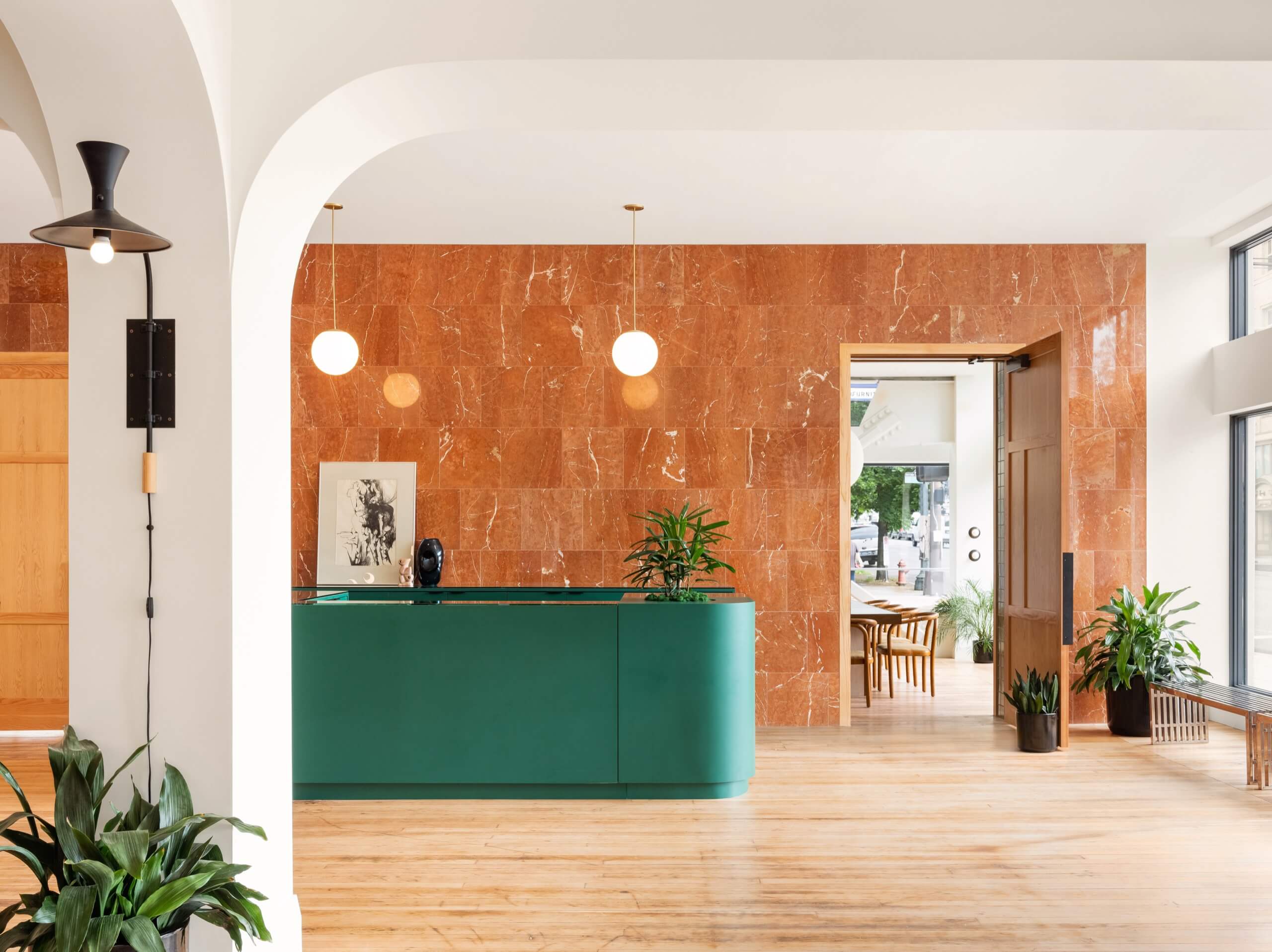 A hotel lobby with a green reception desk, marble wall, and plants.